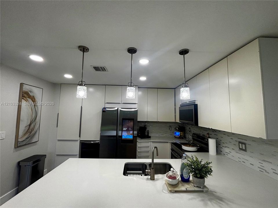 Kitchen featuring slab countertops, flat-panel cabinetry, recessed lighting, glass pendant fixtures, and a dual-basin undermount sink with a gooseneck faucet