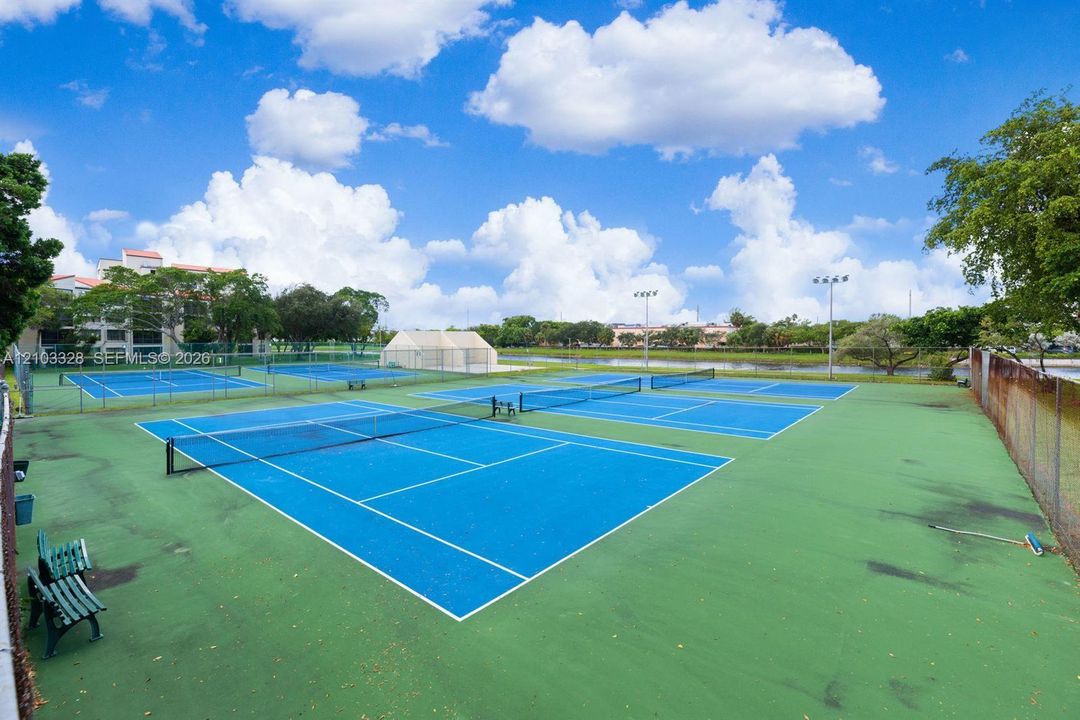 Multi-court tennis facility featuring high-visibility blue surfaces, perimeter fencing, and overhead lighting