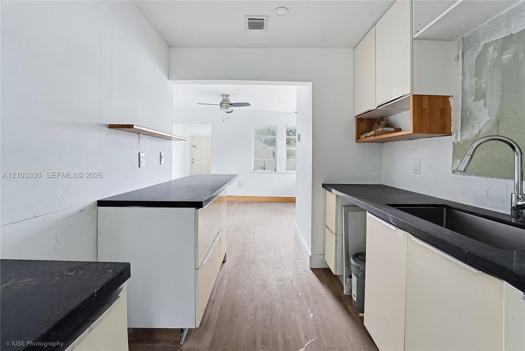 Kitchen featuring white gloss cabinetry, dark stone-finish countertops, wood-finish flooring, a stainless steel undermount sink with a gooseneck faucet, and natural wood floating shelving
