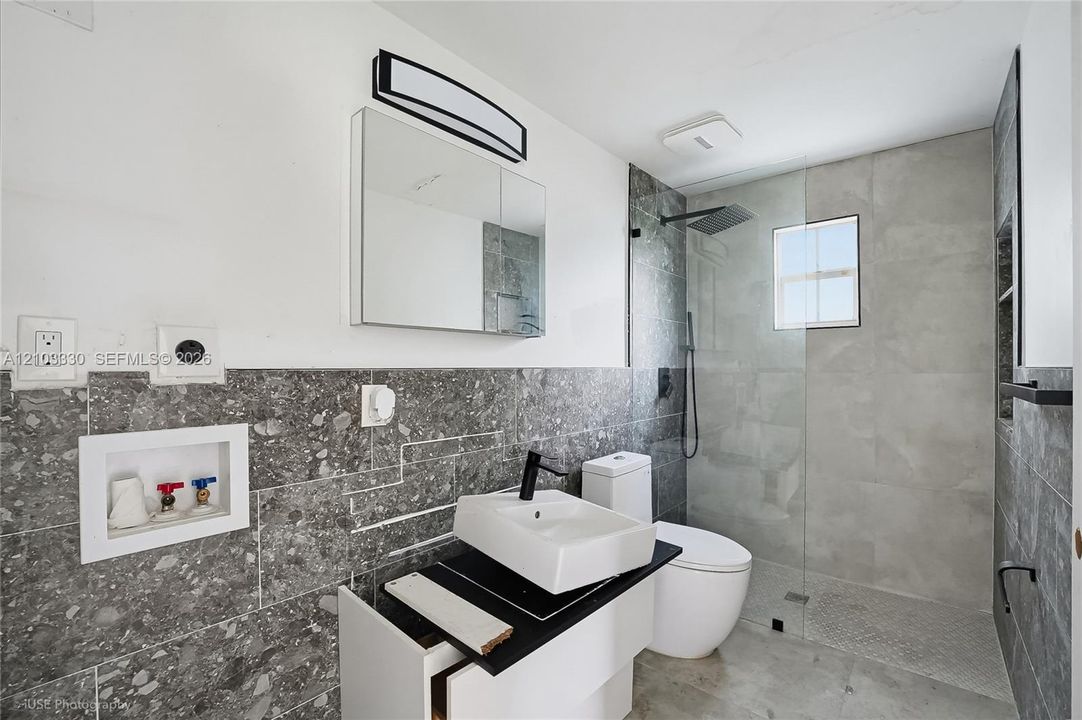 Bathroom featuring a floating vanity with a vessel sink, matte black fixtures, a walk-in shower with a glass panel, and large-format tile wall cladding