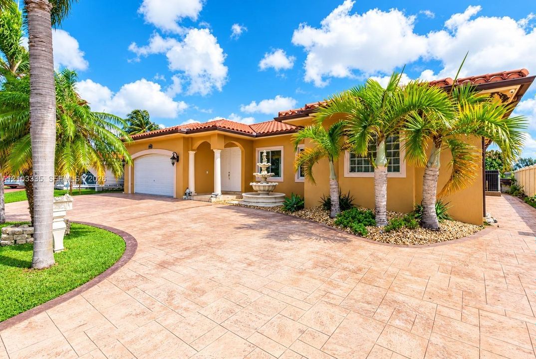 Stucco exterior featuring a red tile roof, multi-car garage, decorative stone fountain, and patterned concrete driveway