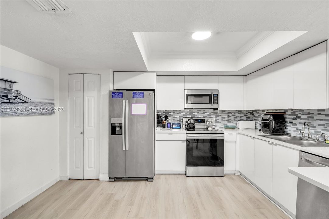 Modern kitchen featuring white cabinetry, stainless steel appliances, a mosaic tile backsplash, and light wood-finish flooring