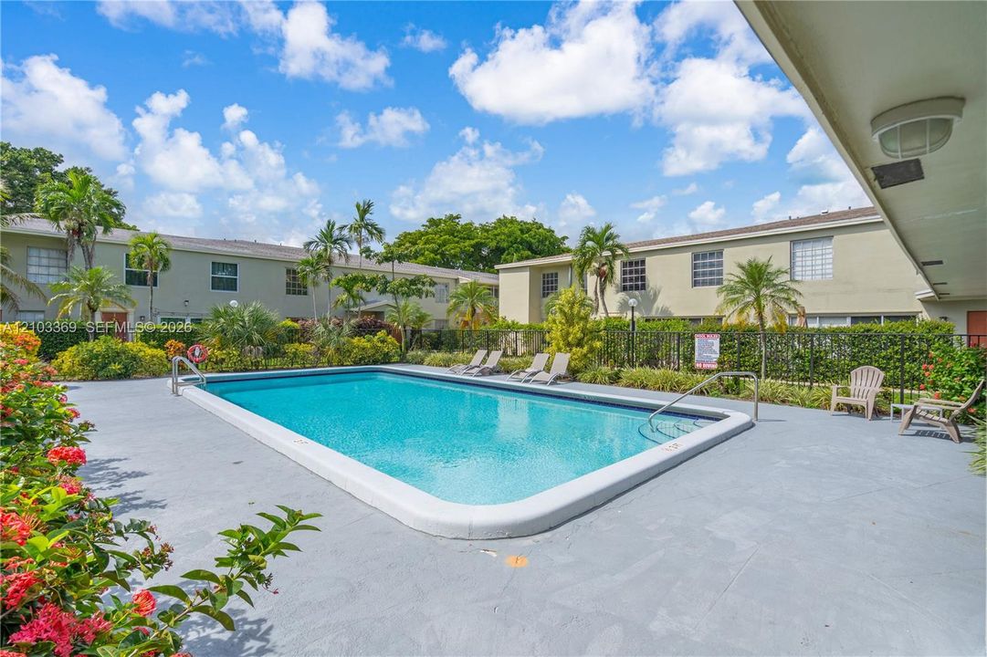 Rectangular swimming pool with a concrete deck, surrounded by lush landscaping and a black metal fence