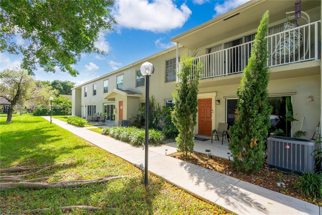 Two-story residential building with private balcony, individual patios, and a landscaped walkway