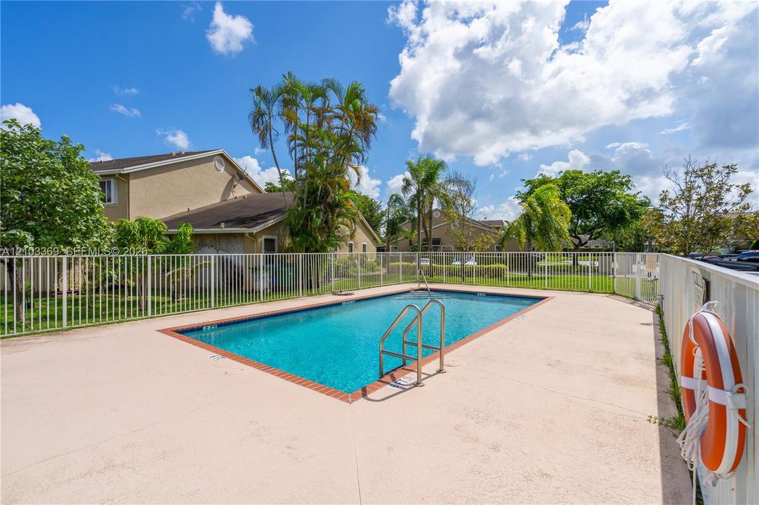 Rectangular swimming pool with integrated steps, surrounded by a concrete deck and a white perimeter fence
