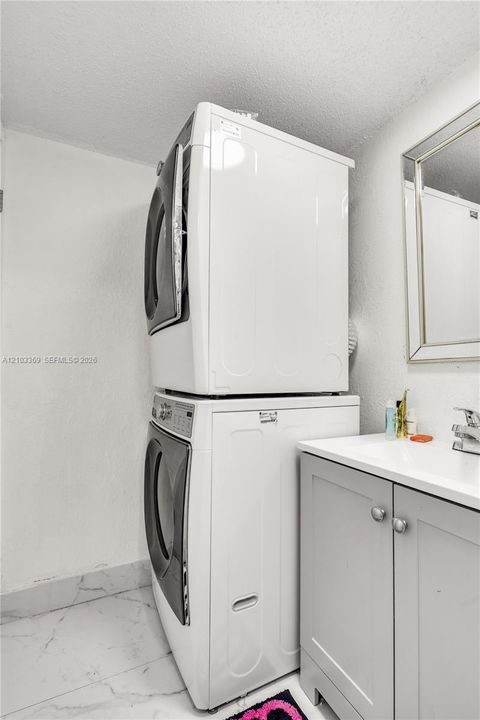 Stackable washer and dryer, vanity with a white countertop, and a framed mirror