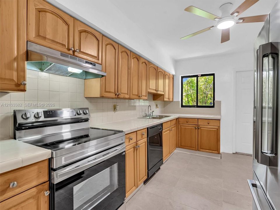 Spaceous kitchen featuring tile countertops, stainless steel appliances, a ceiling fan with integrated lighting, and tile flooring. House for rent in Coral Gables. House for rent listed by Realtor.