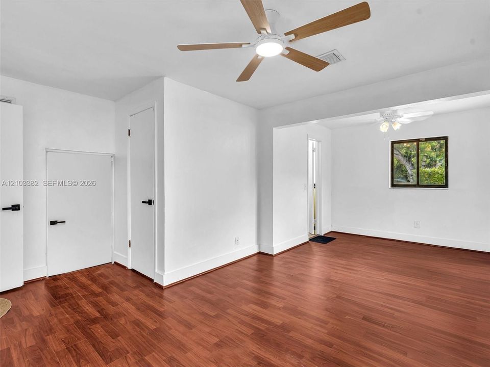 Primary bedroom featuring wood-finish flooring, two ceiling fans with integrated lighting, and doors accented with matte black hardware. House for rent in Coral Gables. House for rent listed by Realtor.