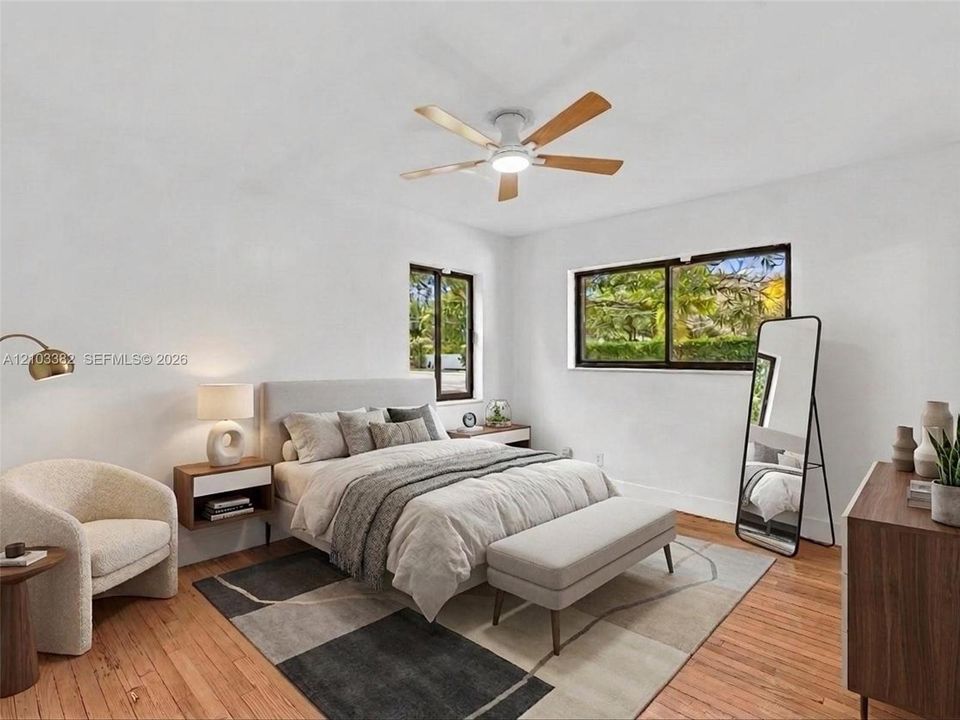 VIRTUAL STAGING. Front west bedroom with en-suite bath and closet. Featuring wood-finish flooring, two sliding windows with dark frames, and a ceiling-mounted fan with integrated lighting. House for rent in Coral Gables. House for rent listed by Realtor.