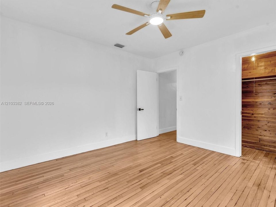 Front east bedroom featuring wood-finish flooring, a ceiling fan with integrated lighting, and a closet finished with wood paneling.House for rent in Coral Gables. House for rent listed by Realtor.