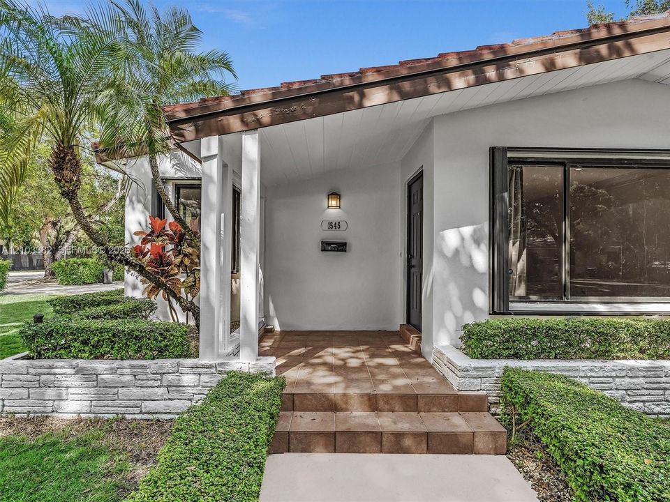 Exterior featuring a covered entryway with ceramic tile steps, white stucco siding, stacked stone landscaping walls, and a large picture window. House for rent in Coral Gables. House for rent listed by Realtor