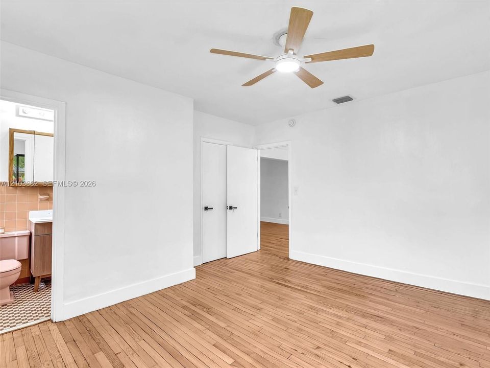West front bedroom with en-suite bath and closet. Wood-finish flooring throughout, ceiling fan with integrated lighting, and white interior doors with matte black hardware. House for rent in Coral Gables. House for rent listed by Realtor.