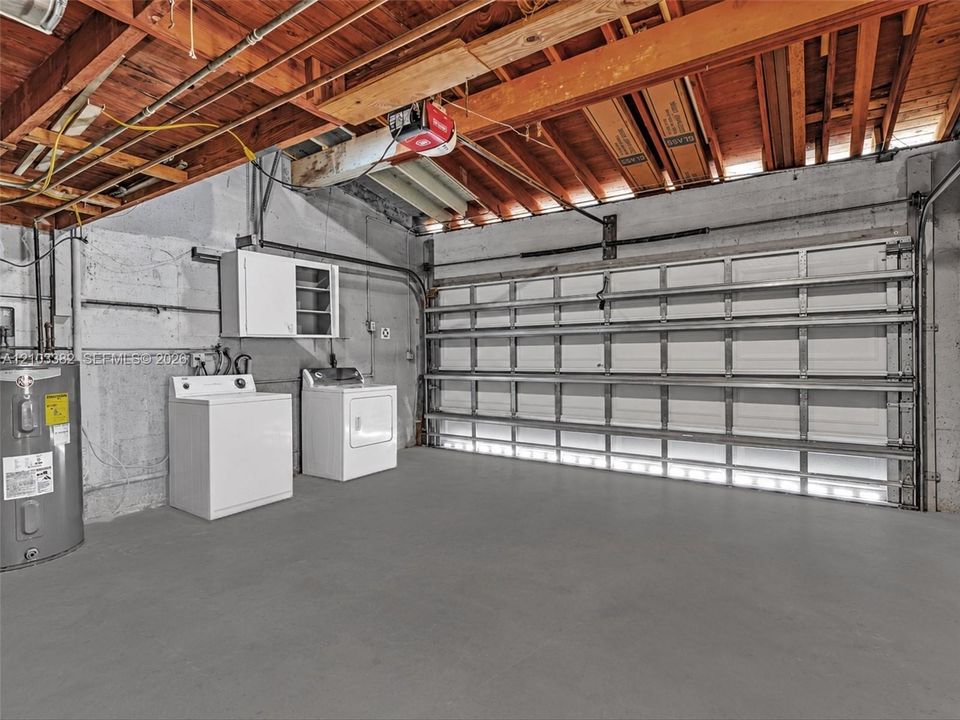 Huge 2 car, attached garage featuring a white sectional roll-up door, exposed wood joist ceiling, concrete walls, and concrete flooring. House for rent in Coral Gables. House for rent listed by Realtor.