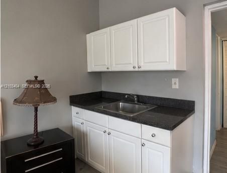 White cabinetry featuring shaker-style doors, dark stone-finish countertop, and stainless steel undermount sink