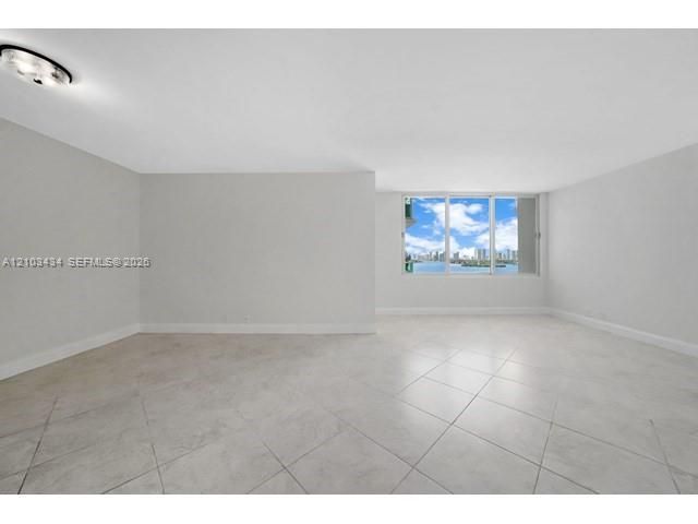 Open-concept room featuring light-toned tile flooring, neutral wall paint, a flush-mount ceiling light, and multi-pane windows providing water and skyline scenery