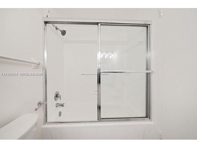 Bathtub and shower combination featuring a chrome sliding glass enclosure, white tile surround, and polished chrome fixtures
