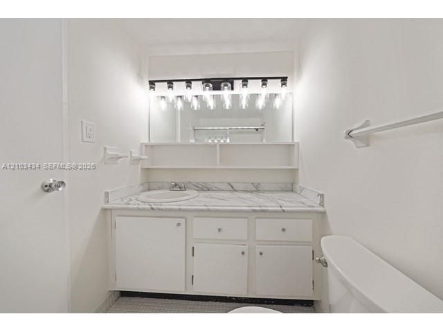 Vanity featuring a stone-finish countertop with an integrated oval sink, white cabinetry with matching hardware, built-in shelving, and a multi-light fixture over a large mirror
