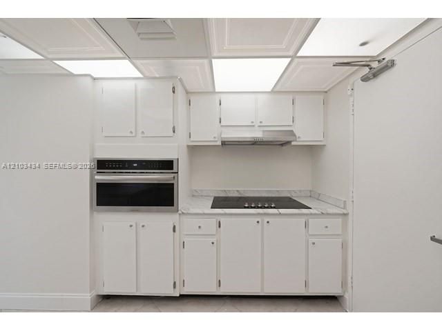 Kitchenette featuring white cabinetry, stone-finish countertops, built-in wall oven, inset stovetop, and stainless steel range hood