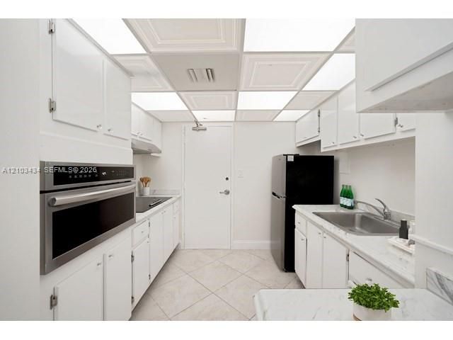 Kitchen featuring white cabinetry, stone-finish countertops, stainless steel wall-mounted oven, drop-in sink with metal faucet, and coffered ceiling panel lighting