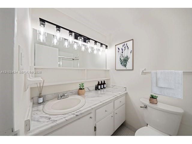 Bathroom featuring a stone-surface vanity countertop, integrated oval sink, white cabinetry with built-in shelving, large wall-mounted mirror, and multi-bulb industrial style lighting fixture