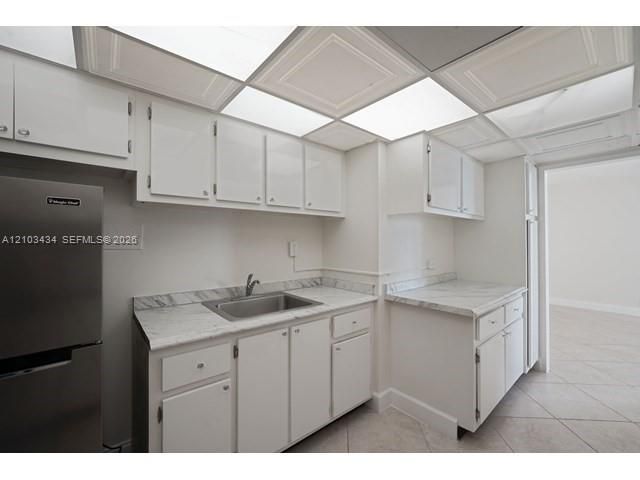 Kitchen featuring white cabinetry, stone-patterned laminate countertops, stainless steel sink, tile flooring, and drop-ceiling panels