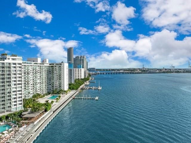 Waterfront high-rise building featuring balconies, a swimming pool, a marina, and hardscaped grounds
