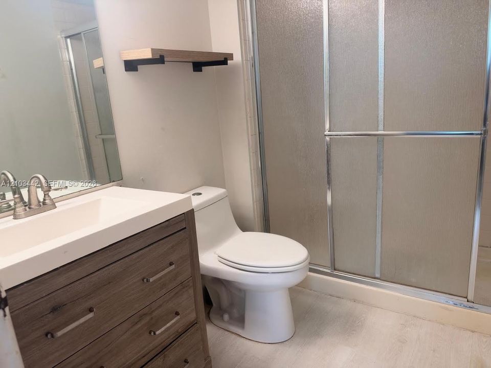 Bathroom featuring a vanity with a wood-finish cabinet and integrated sink, a large wall-mounted mirror, a built-in wood shelving unit, and a walk-in shower with a glass enclosure