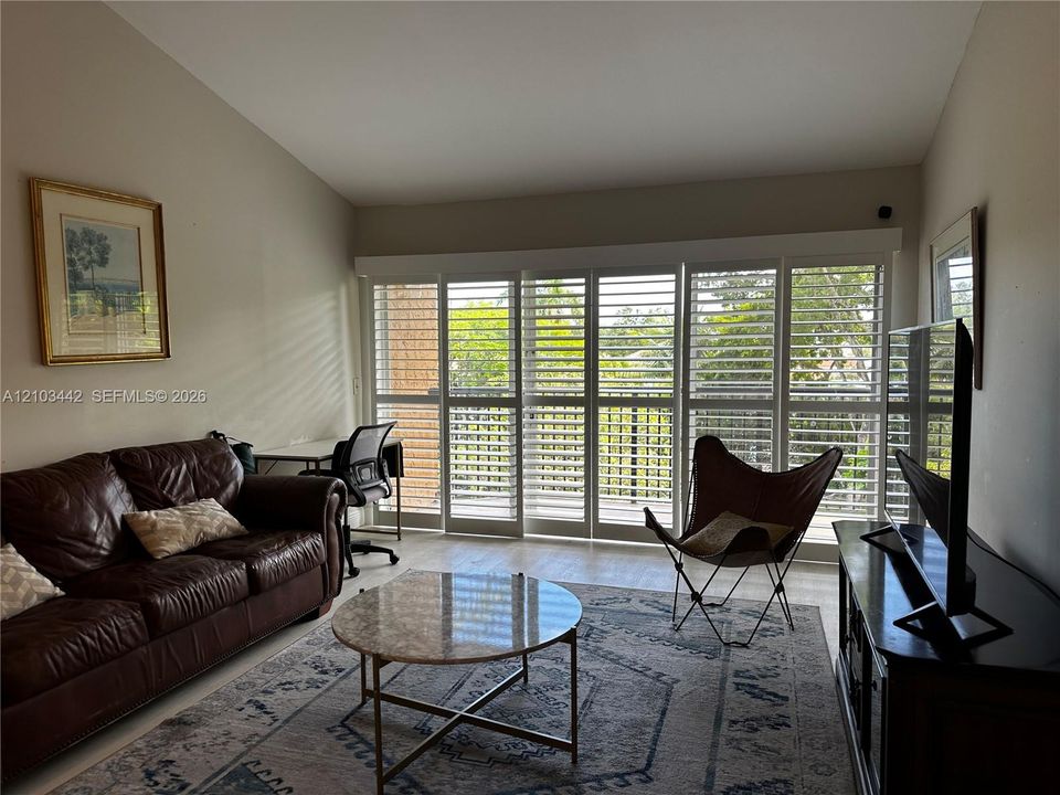 Vaulted ceilings and multi-panel floor-to-ceiling sliding glass doors featuring white plantation-style shutters and wood-finish flooring