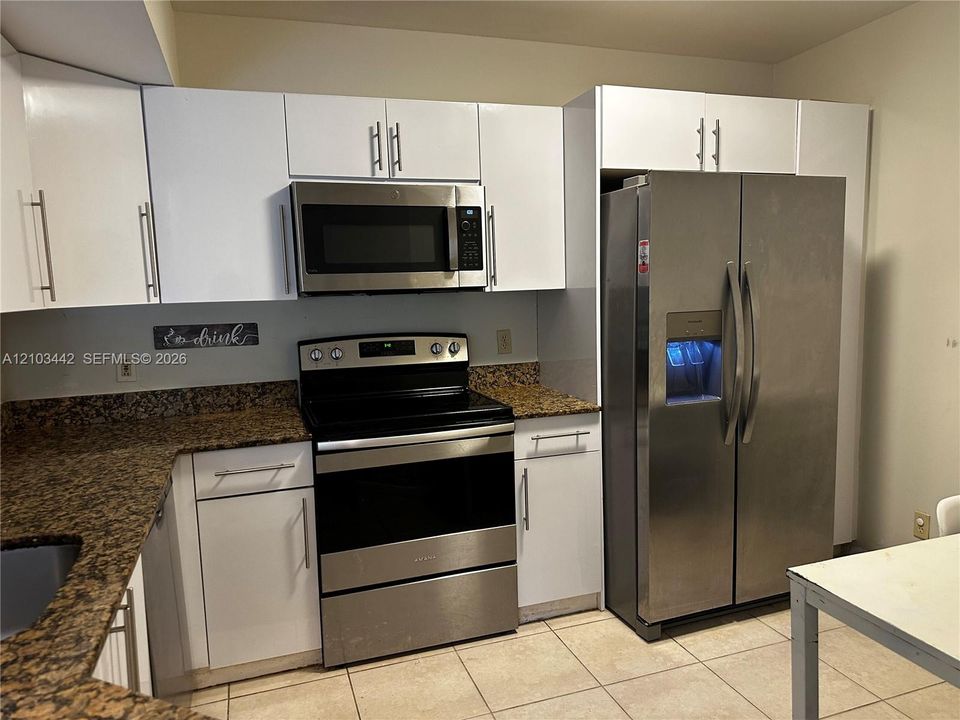 Kitchen featuring white flat-panel cabinetry, stone countertops, and stainless steel appliances including a side-by-side refrigerator, over-the-range microwave, and electric range