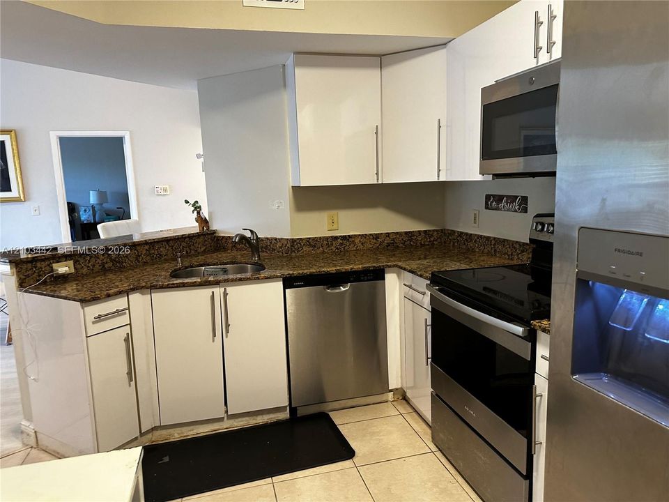 Kitchen featuring white flat-panel cabinetry, stone countertops, stainless steel appliances, a stainless steel undermount sink with a pull-down faucet, and tile flooring