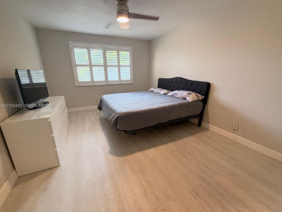 Neutral-toned room featuring light-toned wood-finish flooring, plantation shutters, and a central ceiling fan with an integrated light fixture