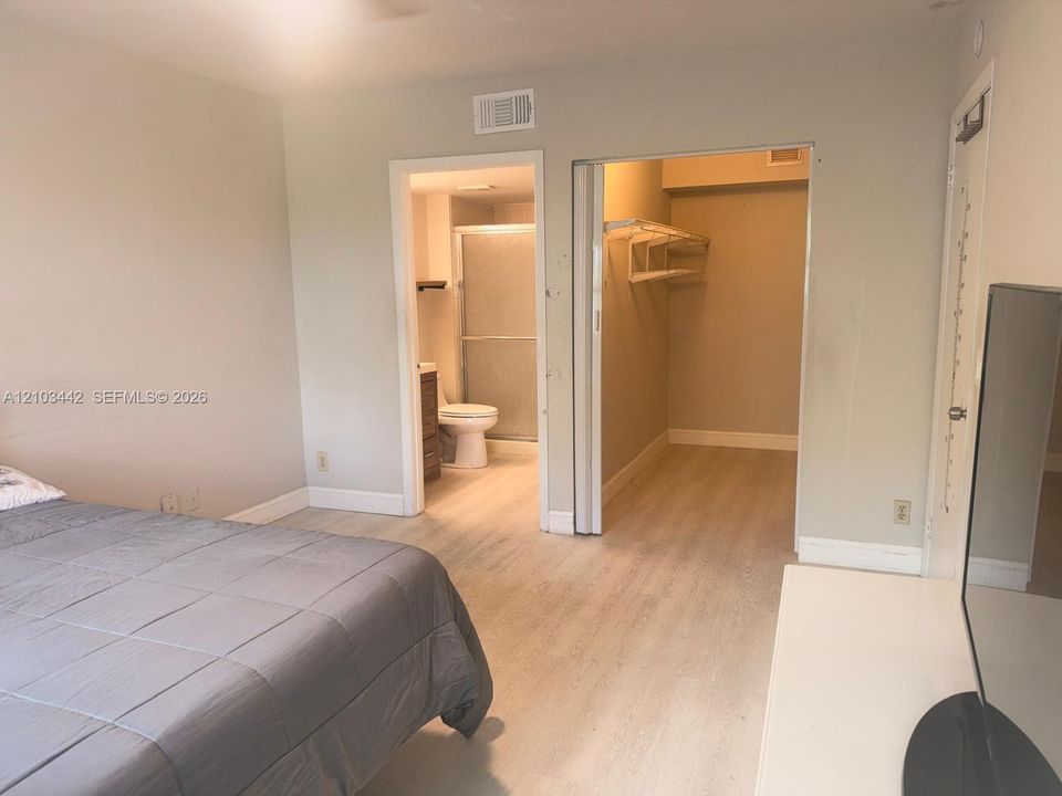 Room featuring wood-finish flooring, a walk-in closet with built-in shelving, and a bathroom equipped with a shower enclosure
