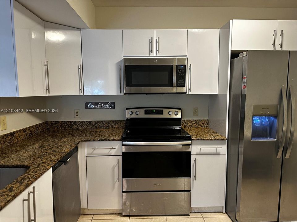 Kitchen featuring white high-gloss cabinetry, stone-finish countertops, stainless steel appliances, and tile flooring