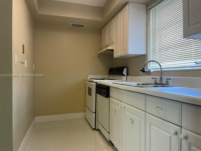 Kitchen featuring white shaker-style cabinetry, a dual-basin stainless steel sink with a high-arch faucet, white appliances, and light-toned tile flooring