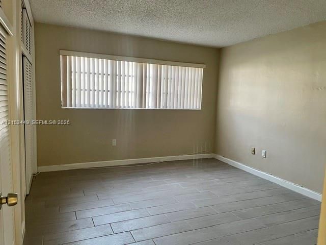 Room featuring large-format tile flooring, textured ceiling, vertical window blinds, and dual bi-fold closet doors