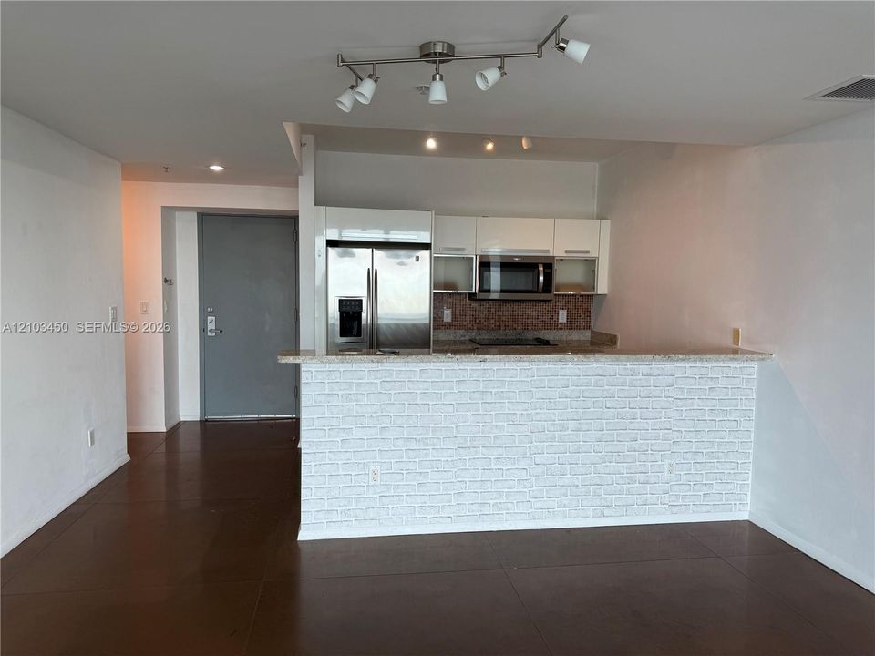Kitchen featuring white flat-panel cabinetry, stainless steel refrigerator and built-in microwave, white stone-patterned breakfast bar, and multi-directional track lighting