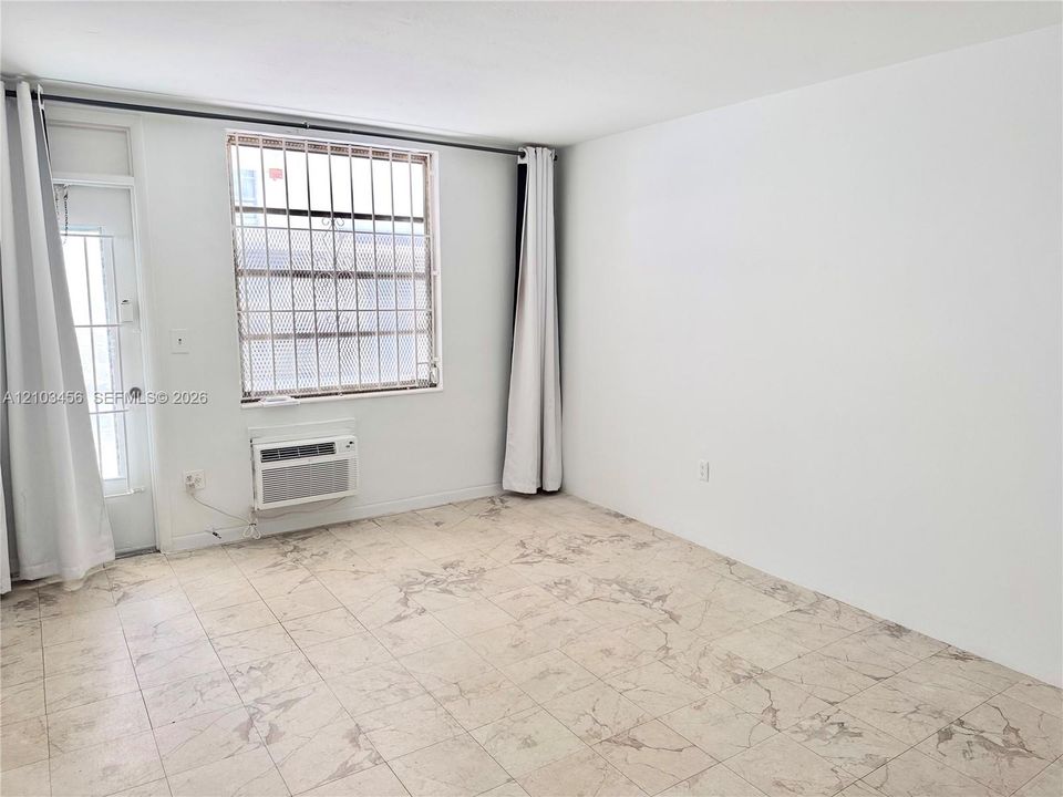 Room featuring stone-patterned tile flooring, a window with metal security bars, an integrated through-wall air conditioning unit, and a glass-paned door