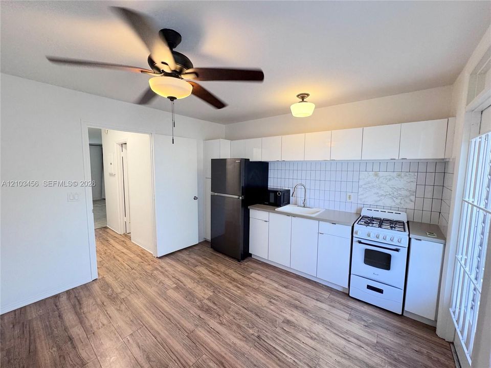 Kitchen featuring white cabinetry, wood-finish flooring, a tiled backsplash, and a ceiling fan with integrated lighting