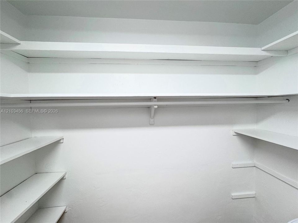 Storage space featuring multiple tiers of built-in shelving and an integrated hanging rod