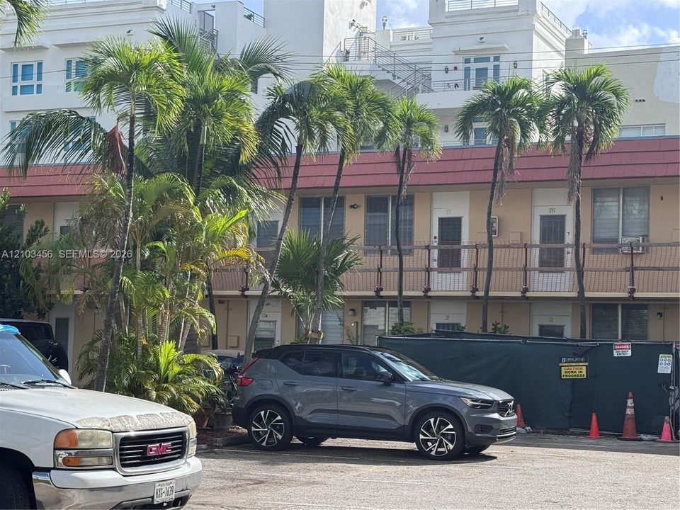 Multi-story building exterior featuring a tiled roofline, second-level railed balcony, and mature palm trees