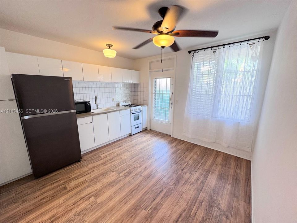 Kitchen featuring white cabinetry, tile backsplash, wood-finish flooring, and a ceiling fan with integrated lighting