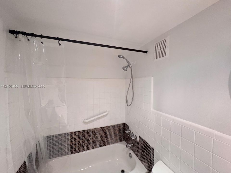 Bathtub featuring white square wall tile, decorative mosaic accent tile, handheld showerhead, and a wall-mounted grab bar