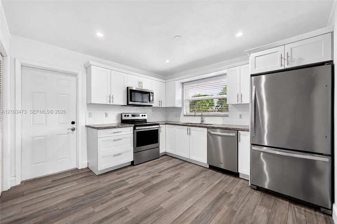 Kitchen featuring white cabinetry, stainless steel appliances, granite-style countertops, white subway tile backsplash, and wood-finish flooring