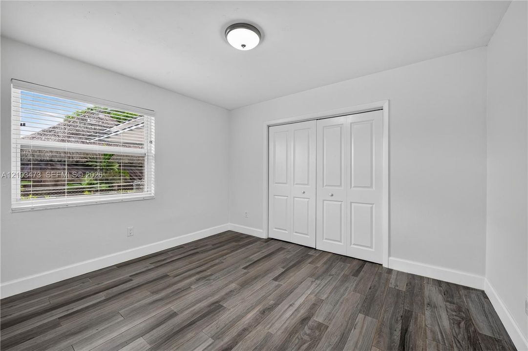 Room with wood-finish flooring, a window with horizontal blinds, and bi-fold closet doors