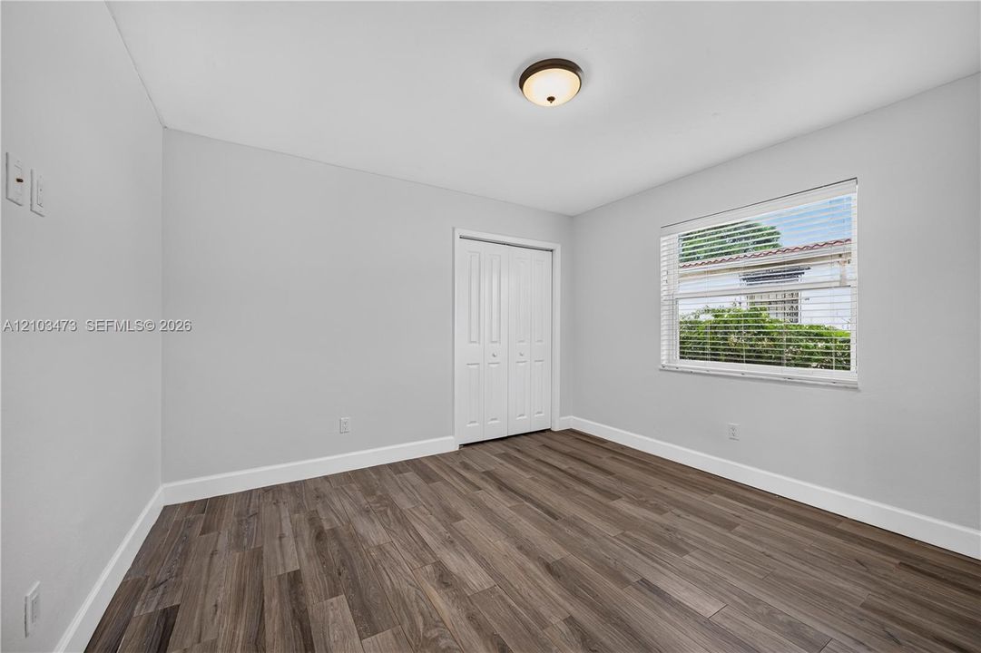 Wood-finish flooring with light gray walls, a window featuring horizontal blinds, and a bi-fold closet door