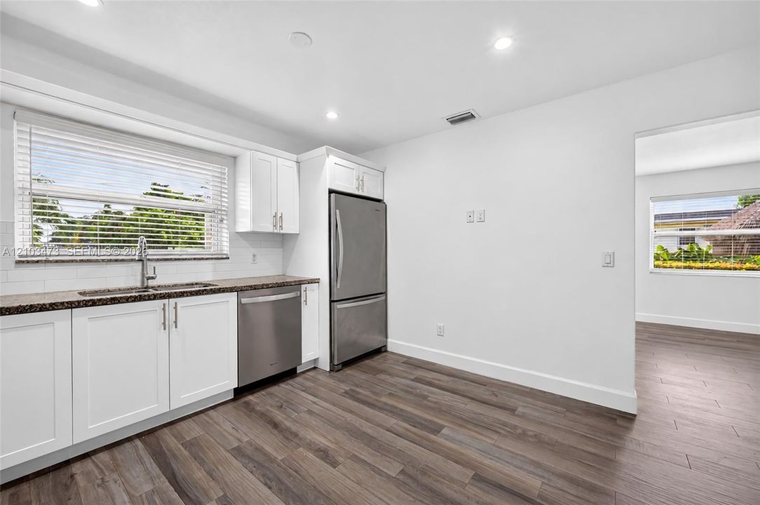 Kitchen featuring white cabinetry, wood-finish flooring, stainless steel appliances, granite-style countertops, and a subway tile backsplash