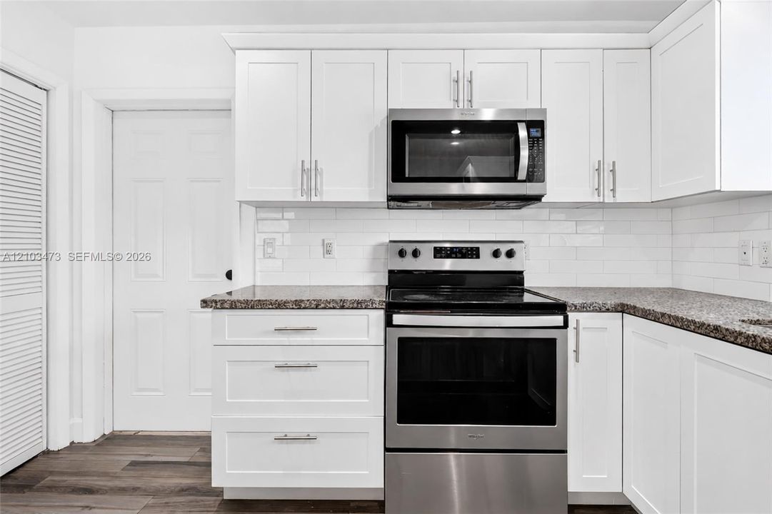 White shaker-style cabinetry with brushed nickel hardware, stainless steel appliances, speckled stone countertops, a white subway tile backsplash, and wood-finish flooring
