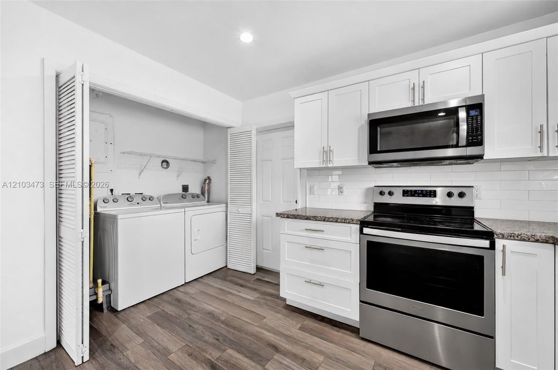 White cabinetry, stainless steel appliances, wood-finish flooring, light-toned countertops, and an in-unit washer and dryer