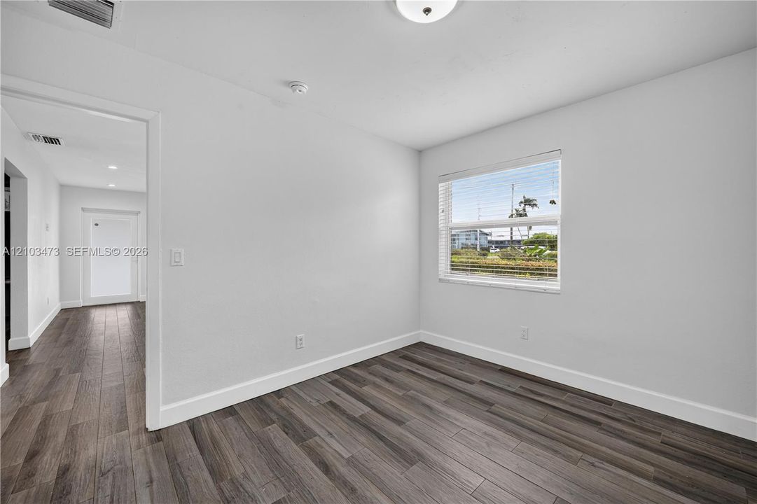 Room with wood-finish flooring, white walls, and a window with blinds