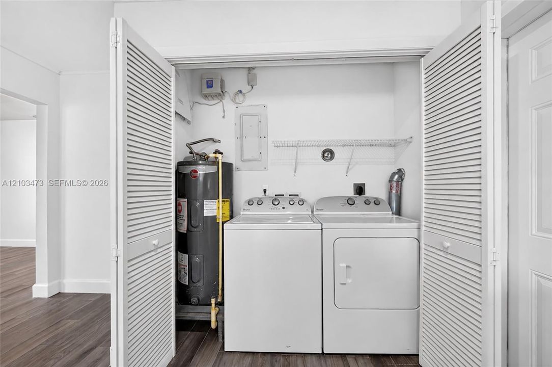 Laundry closet featuring louvered bi-fold doors, white washer and dryer, and a wire storage shelf
